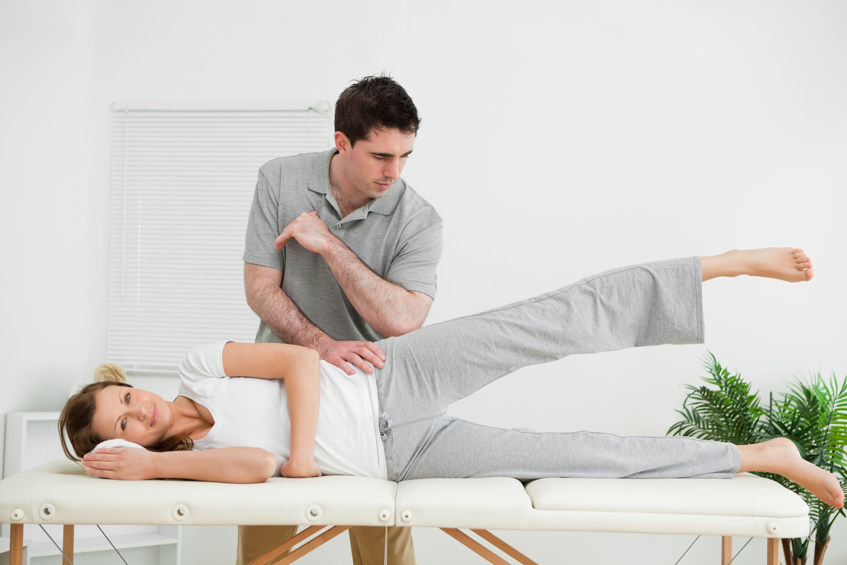 Physiotherapist pressing his elbow on her hip while woman raising her leg in a IMC Physical Therapy Center